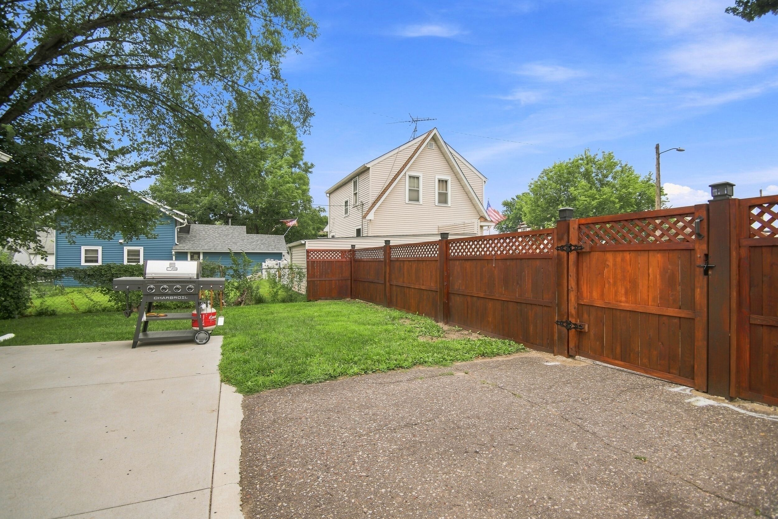 A residential backyard with a wooden fence, a barbecue grill, and a house in the background.