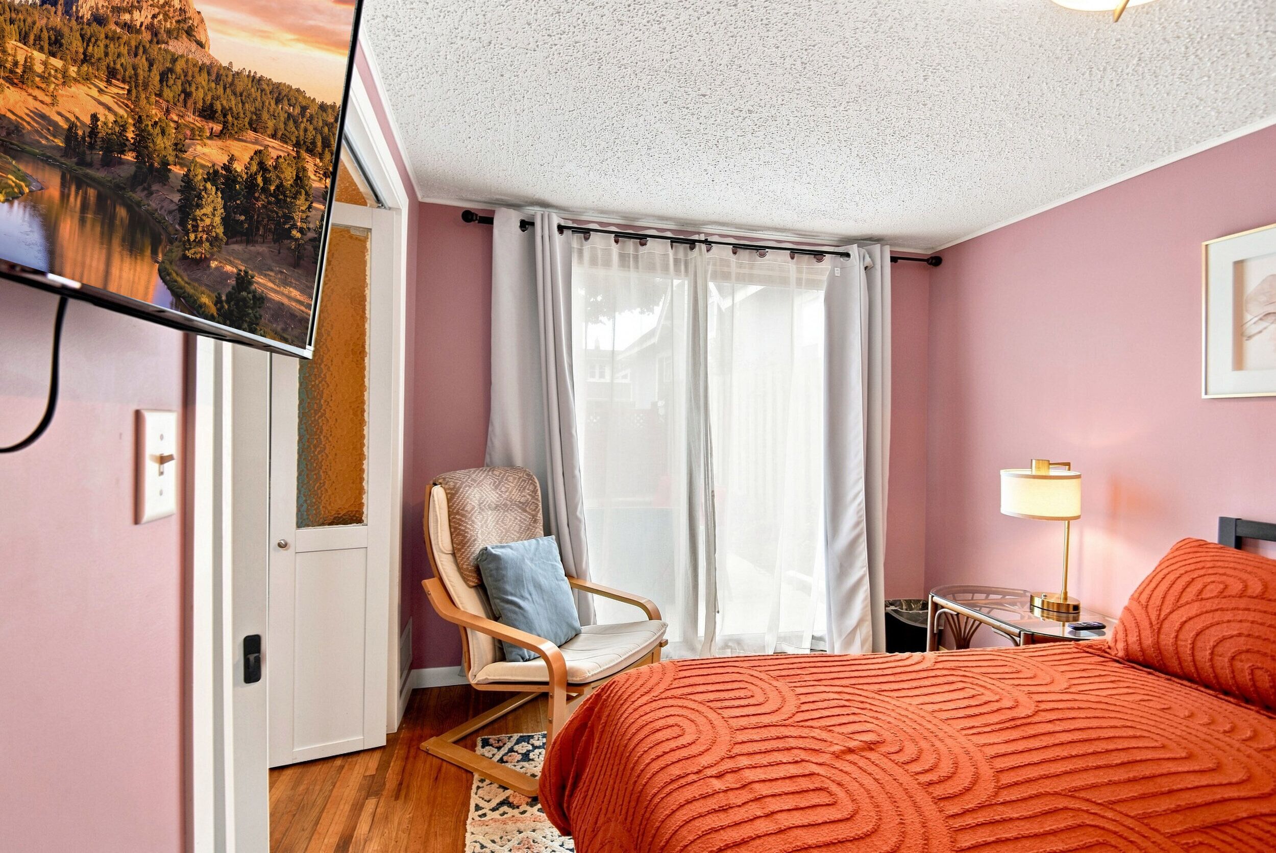 Une chambre à coucher avec un lit, une chaise, une télévision et une fenêtre avec des rideaux.