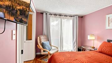 Une chambre à coucher avec un lit, une chaise, une télévision et une fenêtre avec des rideaux.