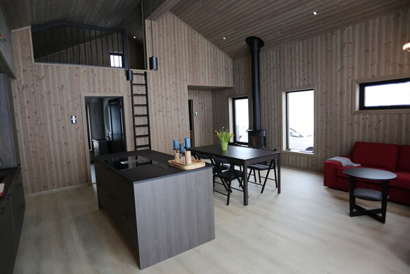 Una cocina moderna con una isla central, un comedor con mesa y sillas, y un sofá rojo.