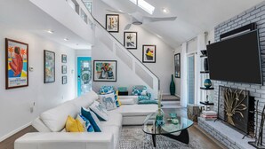 A modern living room with a staircase, a fireplace, and various artworks on the walls. - Beautiful East Hampton Home, Expansive Deck, Private Pool, Indoor/Outdoor... (East Hampton)