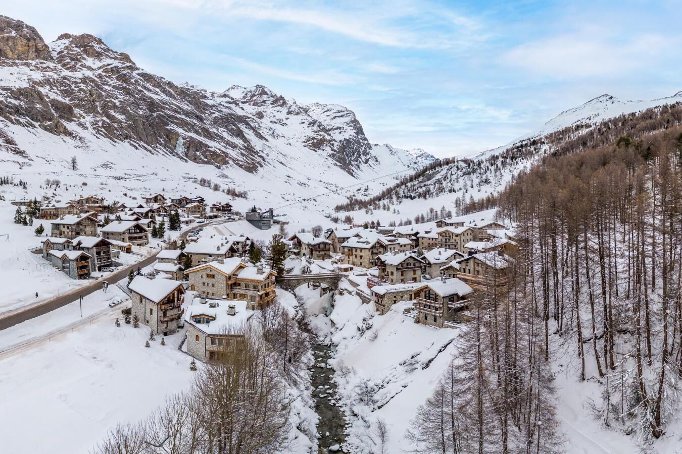 A snow-covered mountain village with traditional wooden buildings, a winding road, and a river.