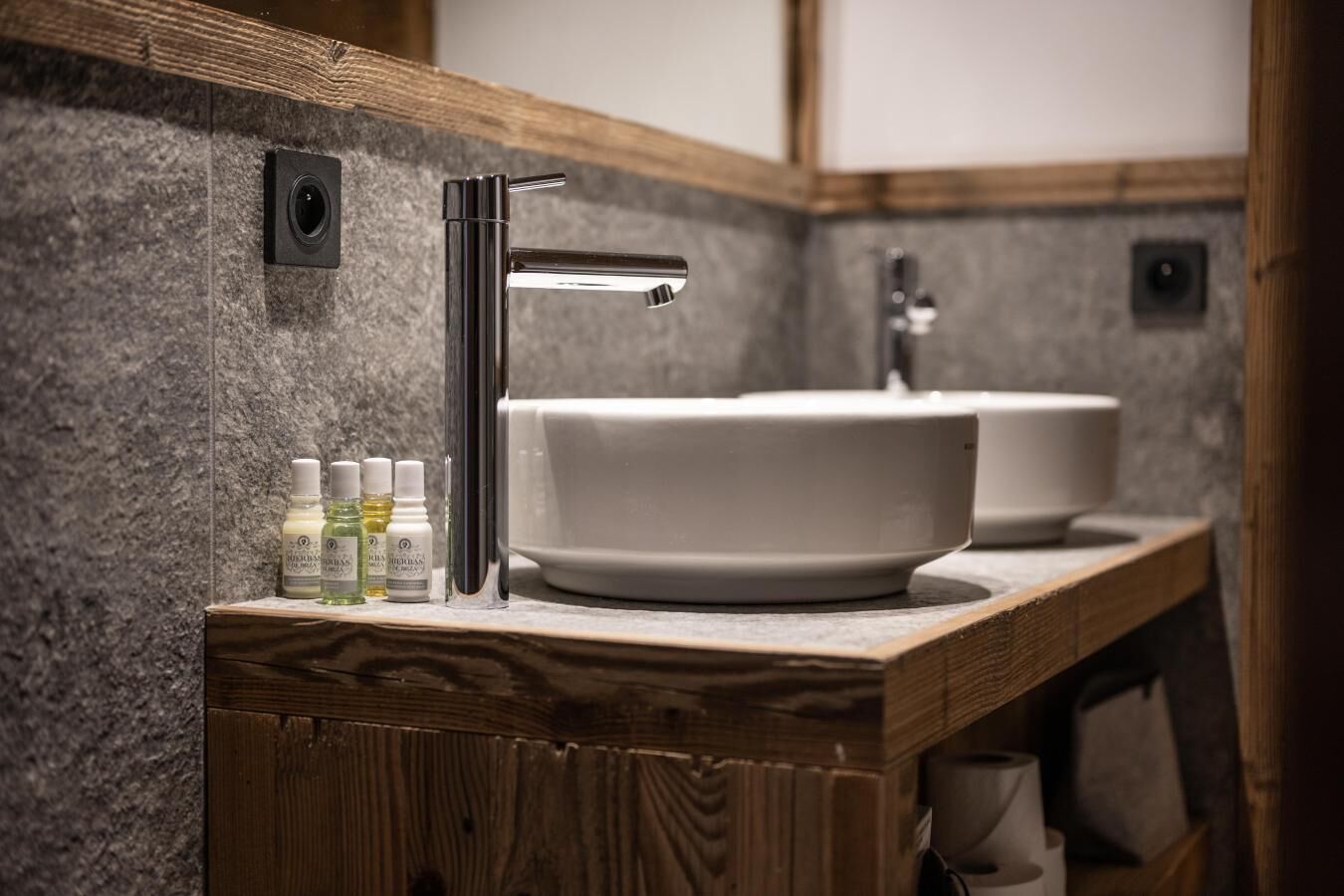 Une salle de bain avec un meuble-lavabo en bois, un lavabo blanc et un miroir. On y trouve des articles de toilette sur le meuble-lavabo.