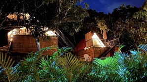 A night scene of a resort with multiple wooden cabins surrounded by dense foliage.