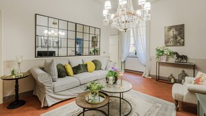 A living room with a sofa, coffee table, and chandelier. There is a large mirror on the wall and a painting above the sofa. - Casa Celeste 3 Bedrooms Apartment with Terrace Inside Lucca (Lucca)