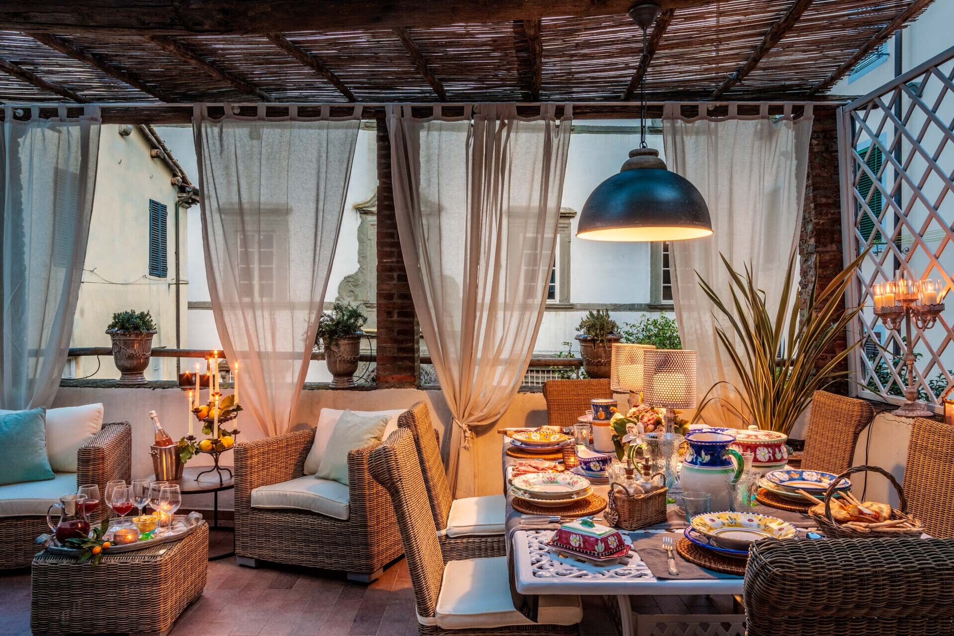 A cozy outdoor seating area with wicker furniture, a table set for a meal, and a hanging lamp.