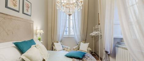 A bedroom with a bed, a chandelier, a window with curtains, and a radiator.