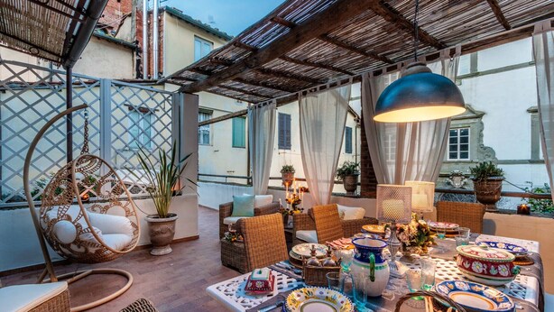 An outdoor dining area with wicker furniture, a hanging chair, and a table set with plates, glasses, and candles. - Casa Celeste 3 Bedrooms Apartment with Terrace Inside Lucca (Lucca)
