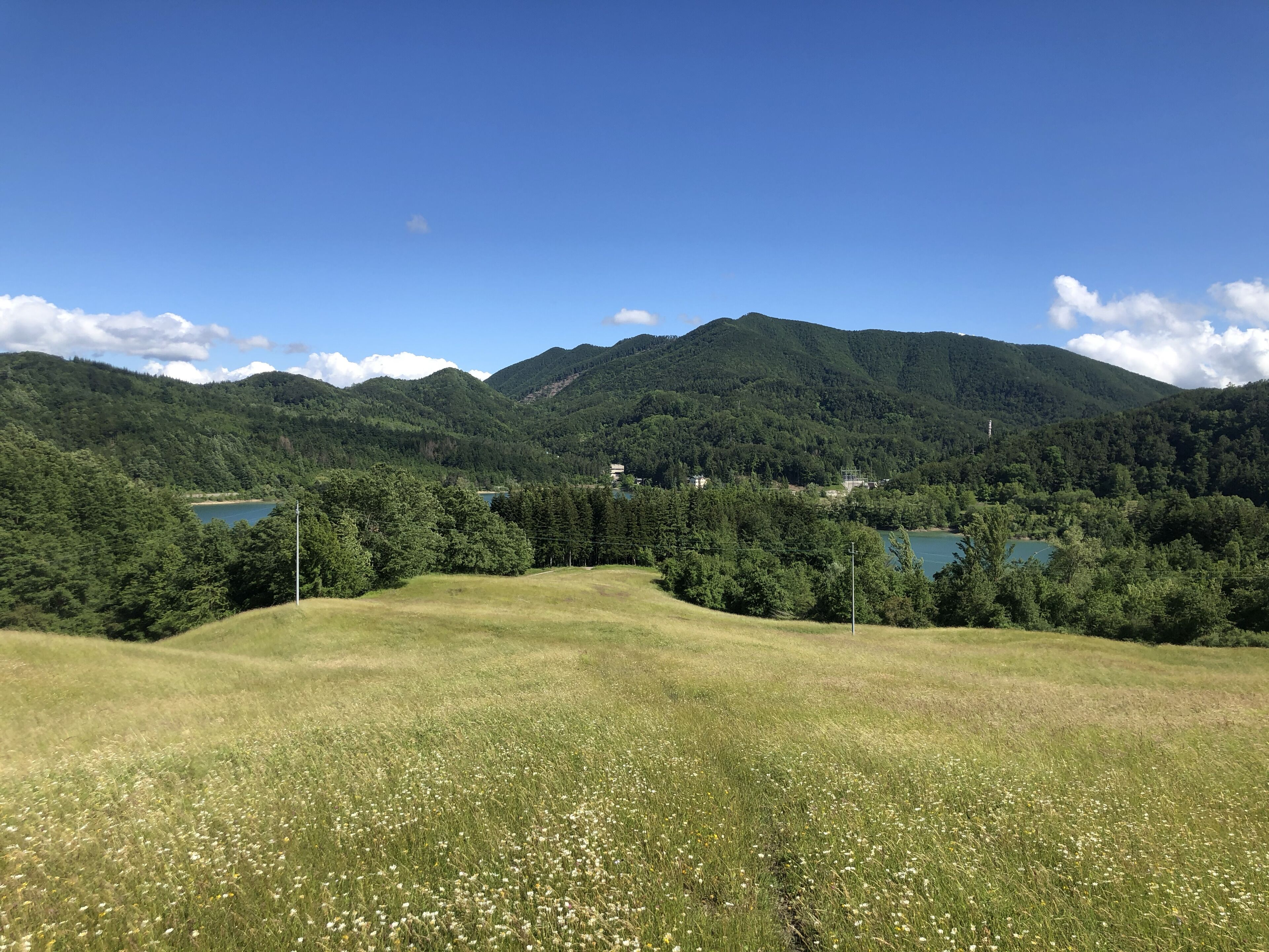 A mountainous landscape with a lake, green fields, and a clear sky.