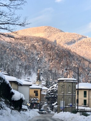 A snow-covered street with buildings, a church, and a mountain in the background. - Appartamento Simona Comfort&relax in Centro Paese (Castiglione dei Pepoli)