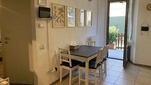 A dining area with a table and chairs, framed artwork on the wall, and a view of the outside. - Appartamento Simona Comfort&relax in Centro Paese (Castiglione dei Pepoli)