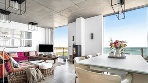 A spacious living room with a large TV, comfortable seating, a dining area, and a view of the sea. - Luxus Beachvilla "the View" (Ostseeresort Olpenitz)
