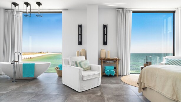 A modern hotel room with a large bathtub, a white sofa, a bed, and a view of the ocean. - Luxus Beachvilla "the View" (Ostseeresort Olpenitz)