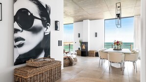 A modern living room with a large painting, wicker baskets, a fireplace, and a dining area with a view of the sea. - Luxus Beachvilla "the View" (Ostseeresort Olpenitz)