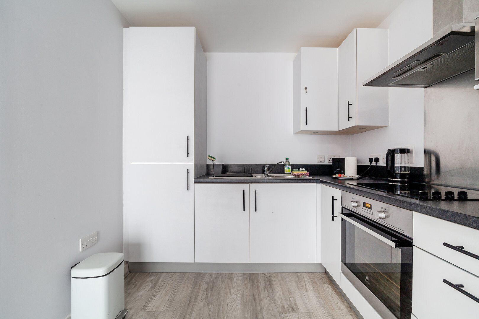 A modern kitchen with white cabinets, a black countertop, and stainless steel appliances.