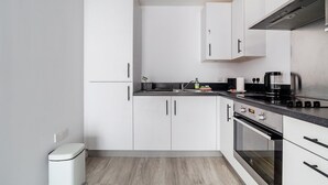 A modern kitchen with white cabinets, a black countertop, and stainless steel appliances. - Riverside Retreat Modern Flat in Brentford (London)