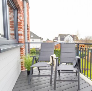 En balkon med to stole, en potteplante og udsigt til huse i baggrunden.