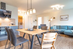 A modern kitchen with a built-in oven, a dining area with a wooden table and chairs, a blue sofa, and a hanging light fixture.
