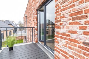 En moderne murbygning med balkon, en potteplante og frit udsyn til gaden.