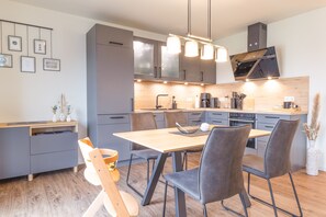 A modern kitchen with grey cabinets, a wooden dining table, and a built-in oven.