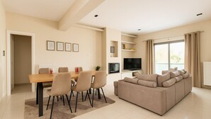 Un salon moderne comprenant un coin repas, un grand canapé, un téléviseur à écran plat et un balcon agrémenté de rideaux.