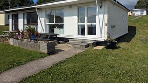 Une maison de plain-pied dotée d’un porche à l’avant, de grandes fenêtres et d’un petit jardin agrémenté de plantes en pot.