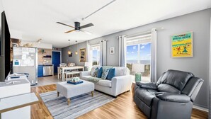 Una sala de estar moderna con un sofá, un sillón de cuero negro, un comedor y una cocina al fondo.