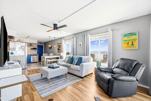 Un salon moderne avec un canapé, un fauteuil en cuir noir, un coin repas et une cuisine en arrière-plan.