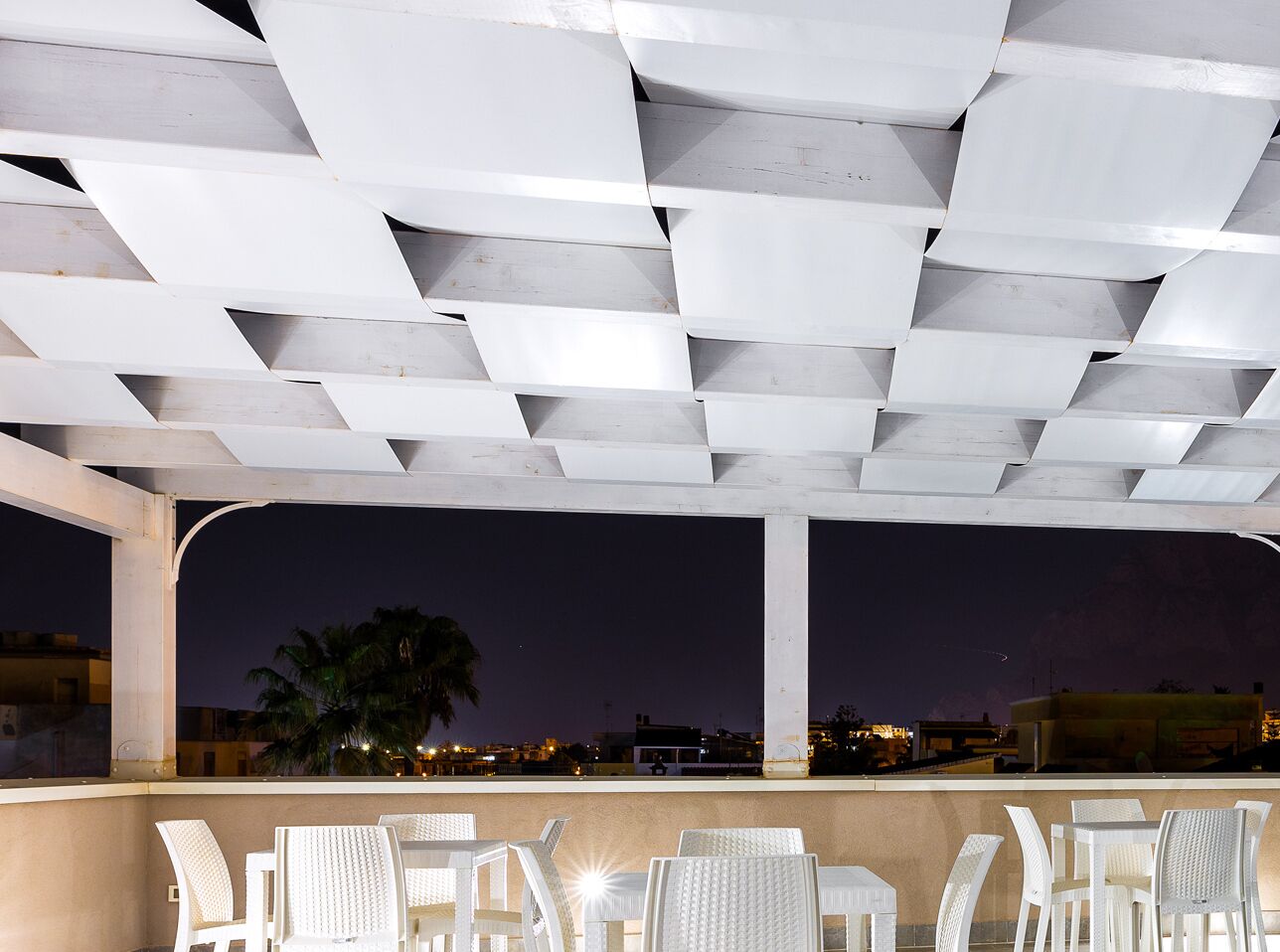 An outdoor seating area with white chairs and a geometric ceiling structure.