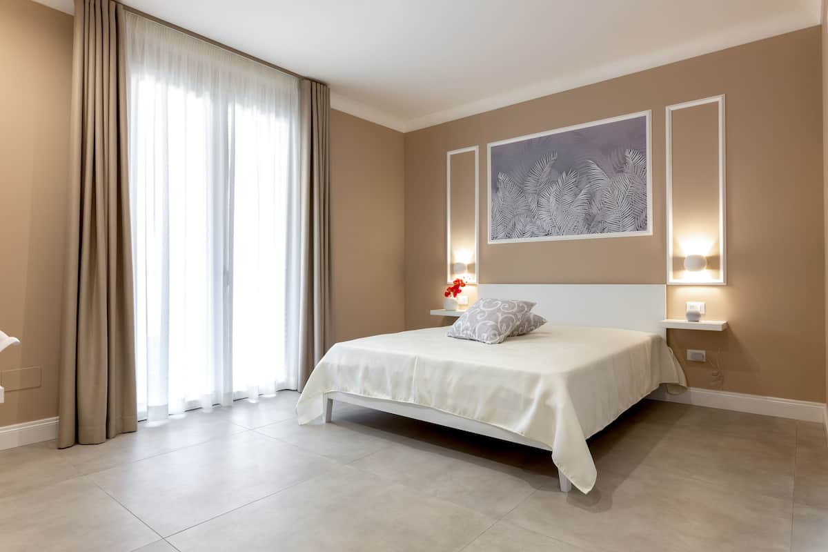 Une chambre moderne avec un grand lit, des murs de couleur beige et une grande fenêtre avec des rideaux.