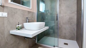 Un baño moderno con ducha envuelta en vidrio, un lavabo blanco con un recipiente y un espejo sobre el lavabo.