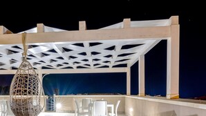 Un espacio al aire libre con sillas y mesas blancas, una silla colgante y un fondo azul.