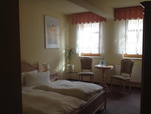 A hotel room with a bed, two chairs, a small table, a potted plant, and a window with curtains. - Hotel zum Stadttor  (Kahla)