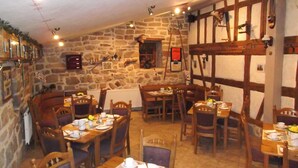 A cozy restaurant with stone walls, wooden beams, and a variety of seating arrangements. Tables are set with plates, cups, and cutlery. - Hotel zum Stadttor  (Kahla)