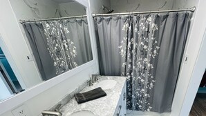 Un baño con dos lavamanos, una cortina de ducha con motivos florales, un espejo y suelo de mármol.