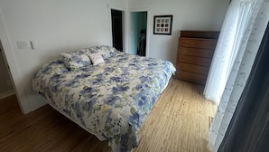 Un dormitorio con cama, ventilador de techo, cómoda y ventana con cortinas.