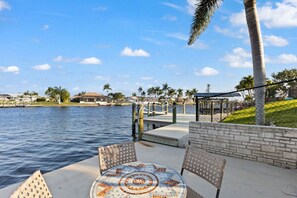 A waterfront patio with a mosaic table, chairs, and a view of the water and distant buildings. - Centrally Located, Waterfront, Modern Home with lots of amenities (Cape Coral)