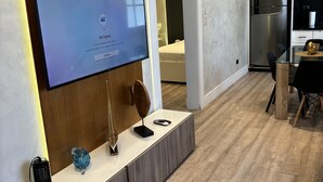 A modern living room with a flat-screen TV mounted on a wooden wall, a sleek black sofa, and a wooden coffee table. - Confy apart CAP CANA (Punta Cana)