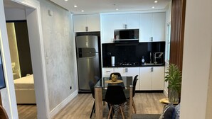 A modern living room with a gray sofa, a glass dining table, and a kitchen area with white cabinets and a stainless steel refrigerator. - Confy apart CAP CANA (Punta Cana)
