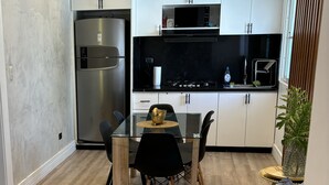 A modern kitchen with white cabinets, a stainless steel refrigerator, a black countertop, and a glass dining table with chairs. - Confy apart CAP CANA (Punta Cana)