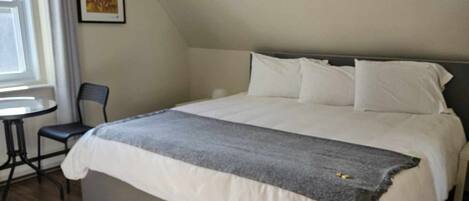 Une chambre avec un grand lit, une chaise, une petite table et une fenêtre avec des rideaux.