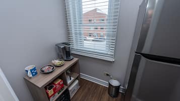 A small kitchenette with a coffee maker, a mug, a plate with cookies, and a trash can.