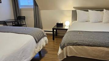 A hotel room with two beds, a small table, a chair, and a window with curtains.