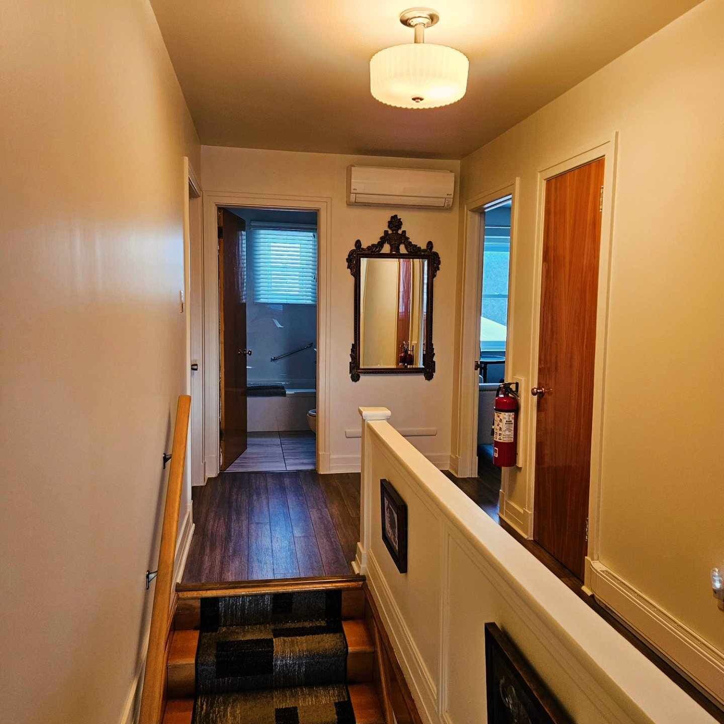 Un couloir étroit avec des marches en bois, une porte blanche et un miroir accroché au mur.