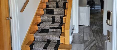 Una escalera con escalones de madera y peldaños cubiertos de alfombra, que lleva a un rellano con una puerta blanca.