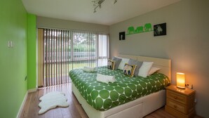 A bedroom with a large bed, a nightstand, a window with blinds, and a green wall. - Two bedroom apartment with balcony dog friendly  (Sandbanks)