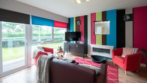 A modern living room with a fireplace, a television, and a large sliding glass door leading to a balcony. - Two bedroom apartment with balcony dog friendly  (Sandbanks)