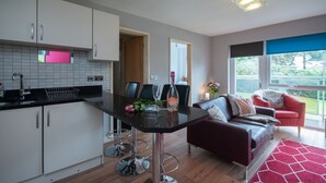 A modern kitchen with white cabinets, a black countertop, and a dining area with a red rug and a sofa. - Two bedroom apartment with balcony dog friendly  (Sandbanks)