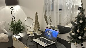 Habitació moderna i ben il·luminada amb un portàtil sobre un escriptori negre de cristall, un xicotet arbre de Nadal i un mirall.