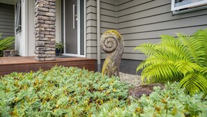 Una casa con un pilastro in pietra, una scultura di un albero a spirale e vegetazione rigogliosa.